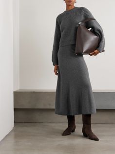 Woman in a gray sweater and midi skirt holding a brown handbag