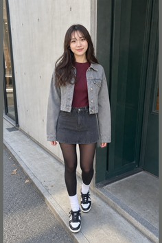 Woman in a denim jacket and skirt with black tights on a street