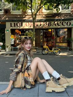 Woman in a plaid shirt and boots sitting on a street in front of a store