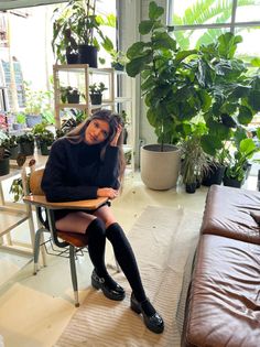 Woman in a black sweater and knee-high socks sitting in a plant-filled room