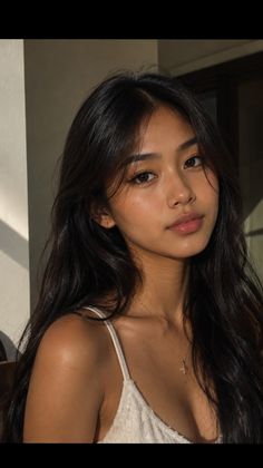 Woman with long dark hair wearing a white top and a cross necklace