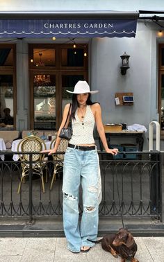 Woman in a white hat and ripped jeans with a small dog outside a cafe