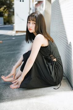 Woman in a black dress with lace detail sitting on the ground outdoors