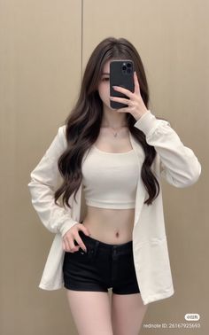 Woman in a white crop top and black shorts taking a mirror selfie