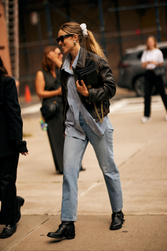 Woman in a leather jacket, striped shirt, and jeans walking on a street