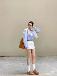 Woman in a blue shirt and white mini skirt with a brown bag and sunglasses