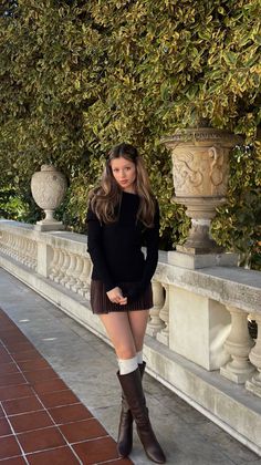 Woman in a black sweater and mini skirt with knee-high boots outdoors