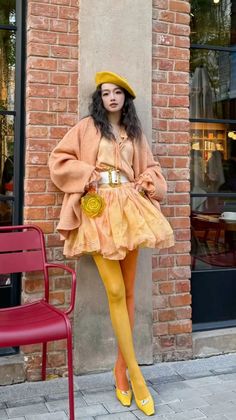 Woman in a yellow beret and colorful outfit posing against a brick wall