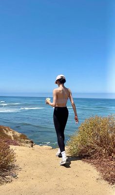 Woman in a sports bra and leggings looking out at the ocean from a cliffside