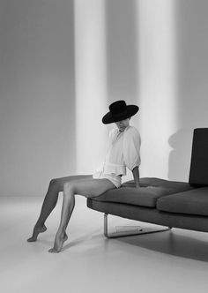 Woman in a wide brim hat and white top sitting on a sofa