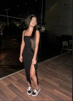 Woman in a black dress with a high slit and sneakers smiling outdoors at night