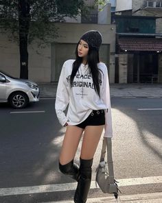 Woman in a beanie, long sleeve shirt, shorts, and thigh-high boots on a street