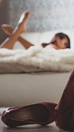 Red heels on the floor with a person lying on a bed in the background