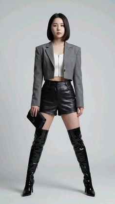Woman in a cropped blazer, leather shorts, and thigh-high boots in a studio