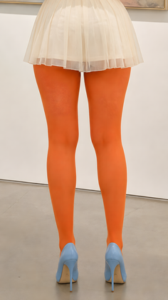 Person in orange tights, a pleated skirt, and light blue high heels standing indoors