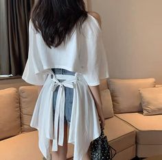 Woman with long dark hair wearing a white tie-back top and denim shorts indoors