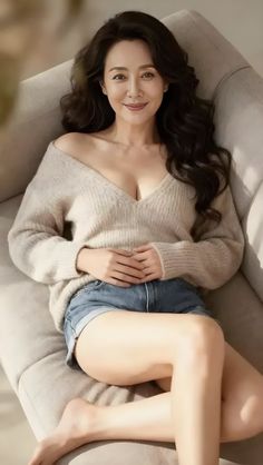 Woman with long dark hair wearing an off-shoulder sweater and denim shorts on a couch