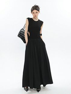 Woman in a black sleeveless dress with cut-outs and a black handbag
