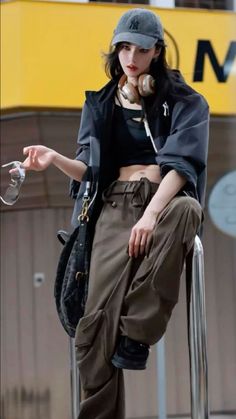 Woman in a baseball cap, crop top, and cargo pants with headphones around her neck