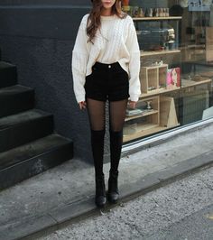 Woman in a white cable knit sweater and black shorts with tights on a street