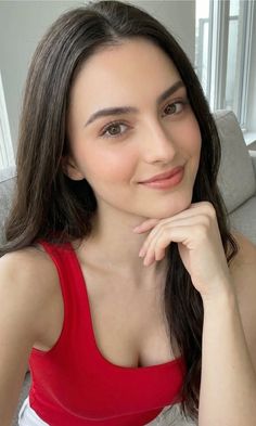 Woman with long dark hair in a red top, smiling and resting her chin on her hand