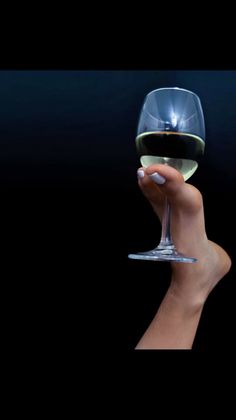 Foot holding a wine glass with white wine against a dark background
