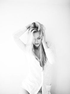 Woman with blonde hair in a white shirt, hands in her hair, looking down