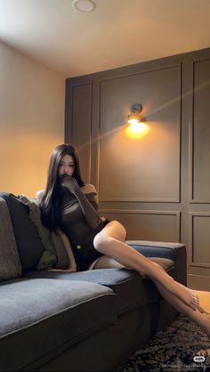 Woman with long dark hair in an off-shoulder top posing on a couch
