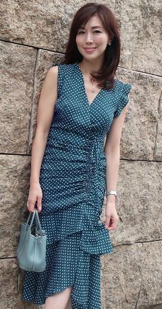 Woman in a dark green patterned midi dress holding a handbag against a stone wall
