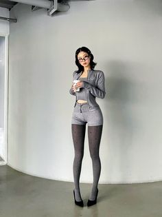 Woman in a gray knit outfit, polka dot tights, and high heels holding a cup
