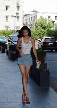 Woman in a white tank top and denim skirt walking on a city street
