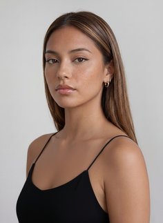 Woman with long hair and freckles wearing a black camisole and gold earrings