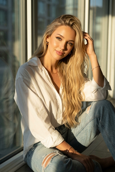 Woman with long blonde hair in a white shirt and ripped jeans, bathed in golden hour light