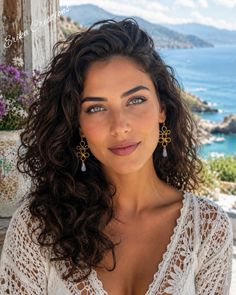 Woman with curly hair wearing a lace top and earrings, with a sea view