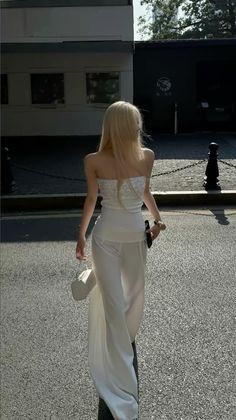 Woman with blonde hair in a white strapless top and pants walking on a street