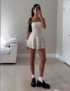 Woman in a polka dot strapless dress and chunky loafers taking a mirror selfie