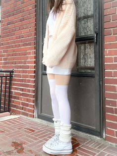 Person in a chunky knit cardigan, white mini skirt, and thigh high socks outdoors