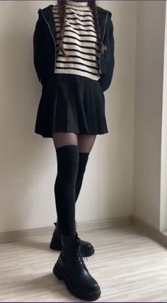 Person in a black skirt, striped sweater, and black boots indoors