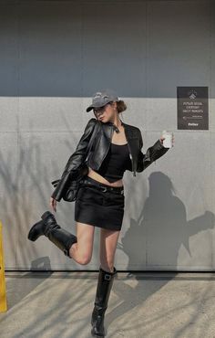 Woman in a black leather jacket and mini skirt posing outdoors with coffee