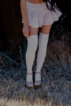 Woman in a white mini skirt and thigh-high socks standing in dry grass