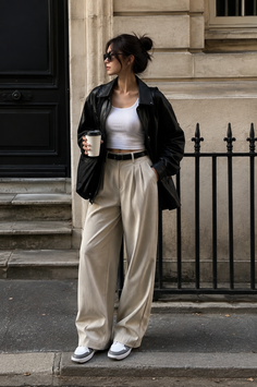 Woman in a black leather jacket and wide leg pants holding a coffee cup on a street
