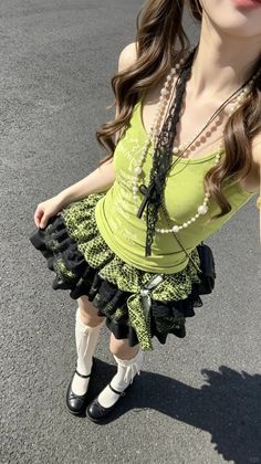 Person in a green tank top and ruffle skirt with pearl necklaces outdoors