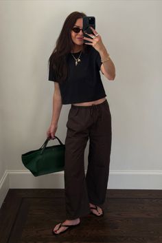 Woman in a black crop top and brown pants taking a mirror selfie indoors