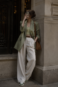 Woman in a green blazer and wide leg pants taking a mirror selfie outdoors