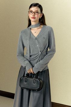 Woman in a gray cardigan and long skirt holding a black handbag indoors