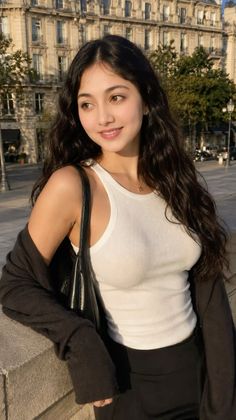 Woman with long wavy hair in a white tank top and black cardigan outdoors
