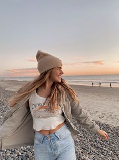 Woman in a beanie and crop top smiling on a beach at sunset