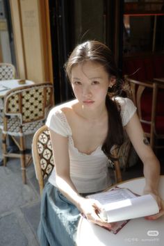 Woman with long hair in a white top sitting at an outdoor cafe
