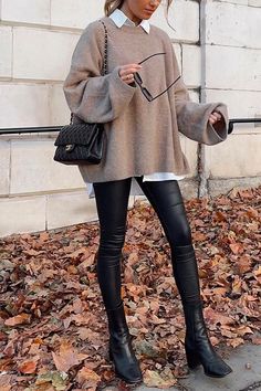 Woman in an oversized sweater and black leggings standing on autumn leaves