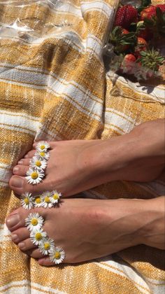 Feet adorned with daisy flowers on a yellow and white striped blanket with strawberries